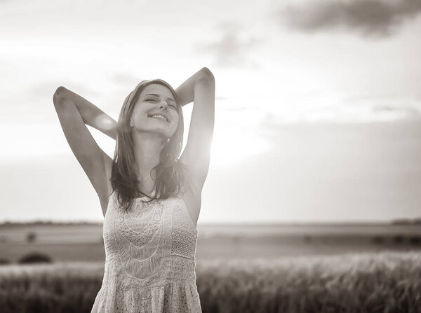 Beautiful adult girl in white dress hands up on countryside with sun ray on background