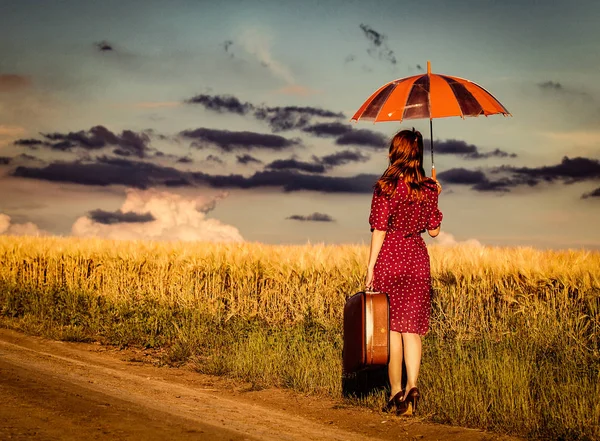 Girl with suitcase and umbrella waking on road — Stock Photo, Image