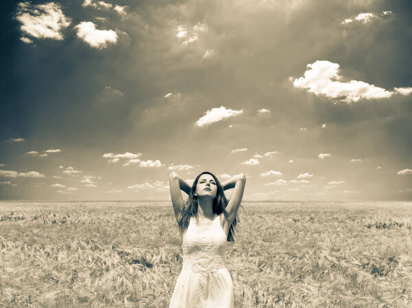 Beautiful girl in white dress stay at wheat field in springtime. Image in sepia color style.