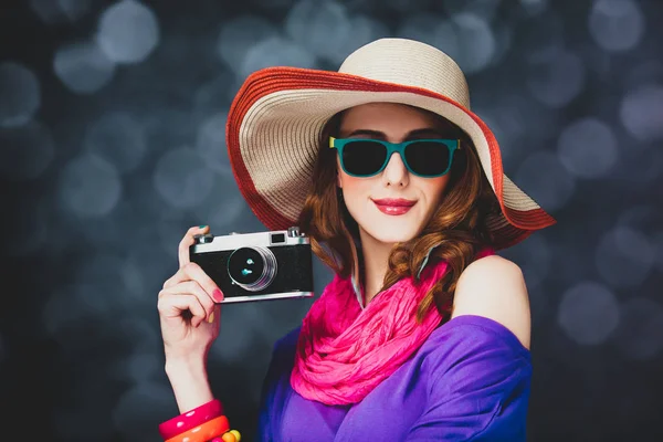 Eleganta rödhårig flicka i hatt och solglasögon med kamera — Stockfoto