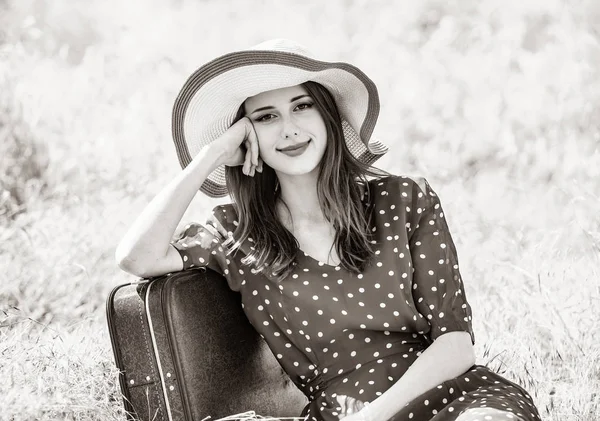 Gadis dengan koper duduk di rumput di pedesaan — Stok Foto