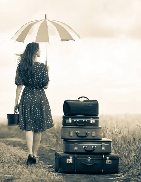 Девушка с чемоданами и зонтиком на сельской дороге во время путешествия — стоковое фото