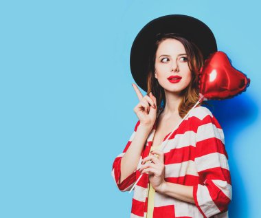 Genç sürpriz Kızıl saçlı beyaz Avrupalı Bayan şapka ve kırmızı çizgili gömlekli kalp şekli oyuncak mavi arka plan ile portresi