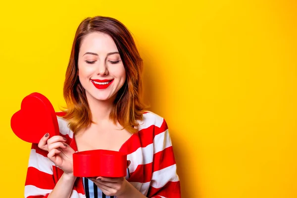 Mulher com caixa de forma de coração no fundo amarelo — Fotografia de Stock