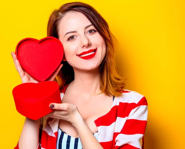 Woman with heart shape box on yellow background — Stock Photo, Image