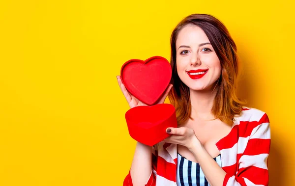 Mulher com caixa de forma de coração no fundo amarelo — Fotografia de Stock