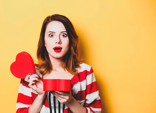 Mulher com caixa de forma de coração no fundo amarelo — Fotografia de Stock