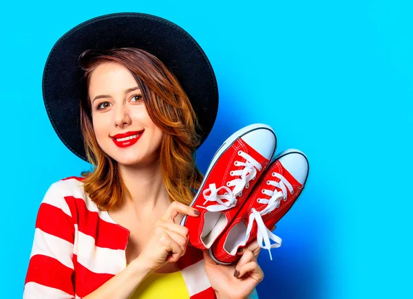 青の背景に赤いための半靴と帽子と赤のストライプのシャツの若い笑顔赤毛白人ヨーロッパ女性の肖像画 — ストック写真