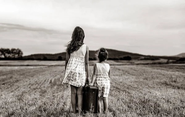 Twee kleine meisjes in klassieke jurk bedrijf koffer — Stockfoto