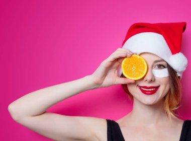 Santa Claus şapka ile portakal izole pembe arka plan üzerinde onun gözünde için göz bandı kullanan kadın. Genelde oldukları gibi doğal ve gerçek erkek portresi gibi görünüyor