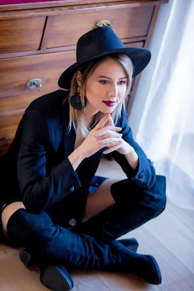 Fekete kalapot és ruhát a padlón ülő lány. — Stock Fotó