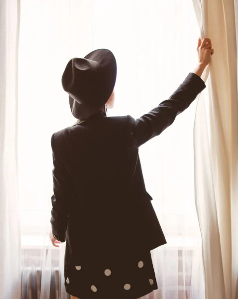 Junges Mädchen in schwarz bleibt in der Nähe des Fensters. — Stockfoto