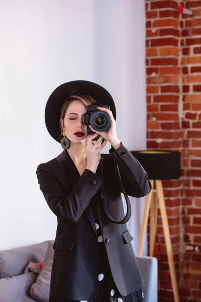 Meisje in een zwarte jurk en muts met camera — Stockfoto