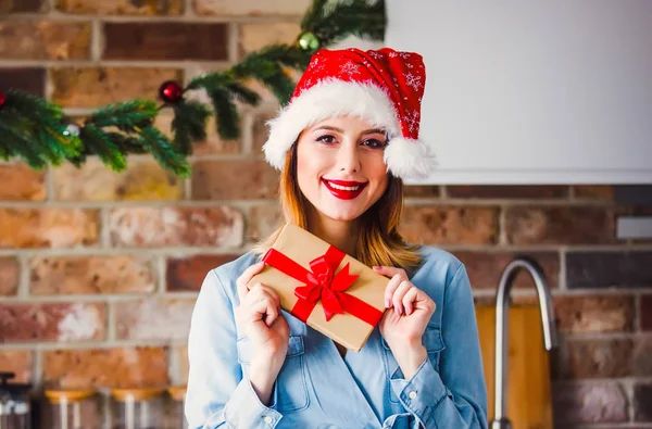 贈り物にキッチンでサンタ クロースの帽子の美しい若い女性 クリスマスの時期 — ストック写真