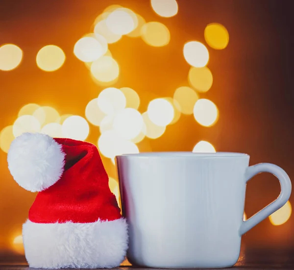 Fehér Csésze Tea Vagy Kávé Mikulás Kalap Karácsonyi Fények Háttérben — Stock Fotó