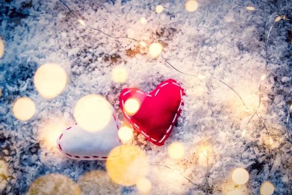 Dos juguetes en forma de corazón y luces de hadas sobre fondo de nieve —  Fotos de Stock