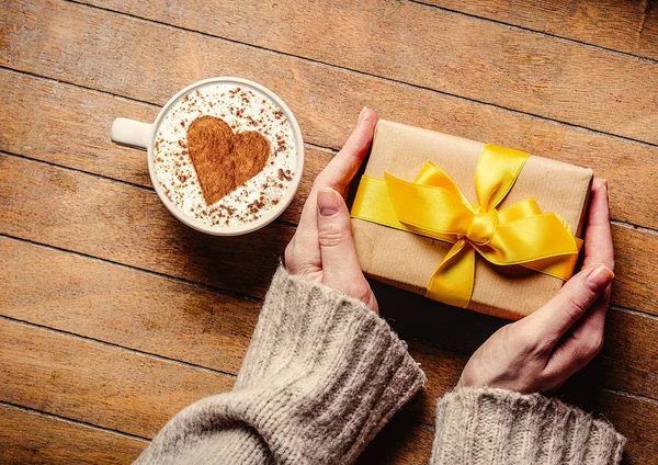 Женские руки с подарочной коробкой и чашкой кофе — стоковое фото