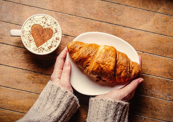 Woman hands holding croissaint near cup of coffee — Stock Photo, Image