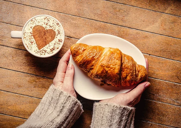 Mani di donna che tengono croissaint vicino a tazza di caffè — Foto Stock