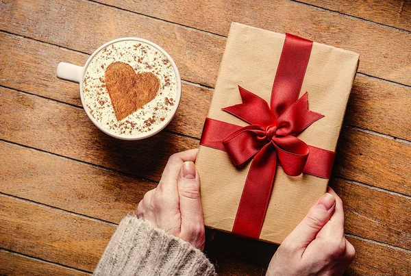 Female hands holding gift box and cup of coffee — Stock Photo, Image