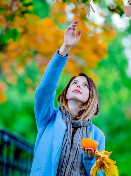 Mujer sosteniendo hojas de arce amarillo y calabaza en autum park — Foto de Stock