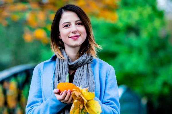 Woman holding yellow maple tree leaves and pumkin in autum park — Stock Photo, Image