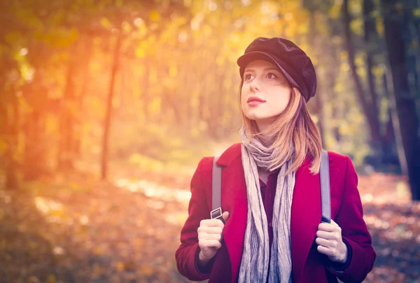 Donna in cappotto rosso e zaino hanno un riposo nel parco autunnale — Foto Stock