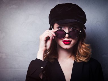 Siyah şapka ve güneş gözlüğü gri arka plan üzerinde elbise tarzı Kızıl saçlı kız