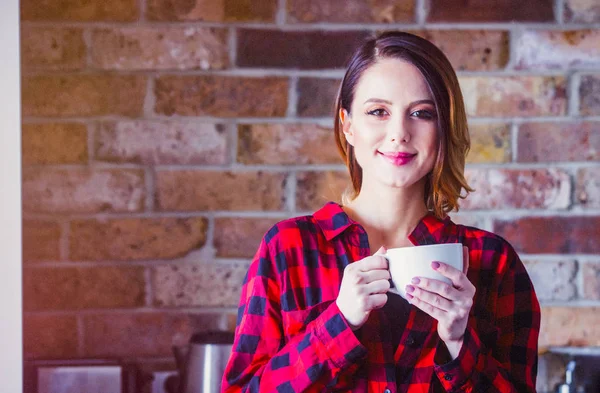 赤シャツのキッチンで紅茶やコーヒーの立っているカップで若い女性の肖像画 朝の時間 — ストック写真