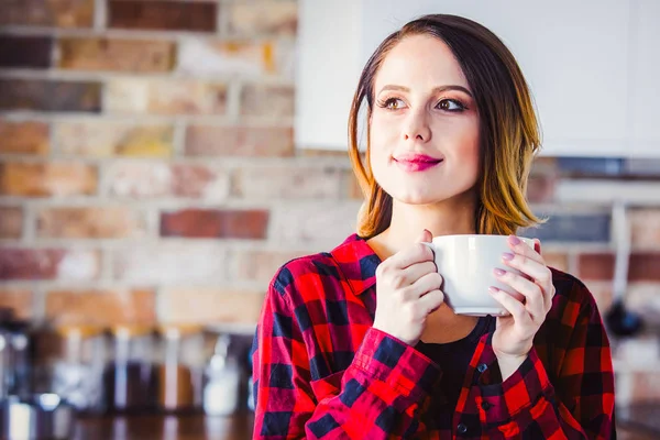 赤シャツのキッチンで紅茶やコーヒーの立っているカップで若い女性の肖像画 朝の時間 — ストック写真