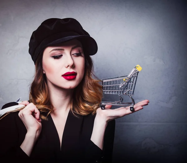 ショッピング バッグと灰色の背景にカートの帽子スタイルの赤毛の女の子 — ストック写真