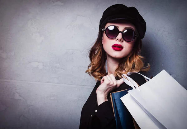 Stijl Roodharige Meisje Muts Met Shopping Tassen Zonnebrillen Grijze Achtergrond — Stockfoto