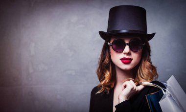 Tarzı Kızıl saçlı kız gri arka plan üzerinde alışveriş torbaları ile üst şapka