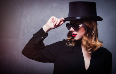 Silindir şapka ve güneş gözlüğü gri arka plan üzerinde stil ve gizemi Kızıl saçlı kız