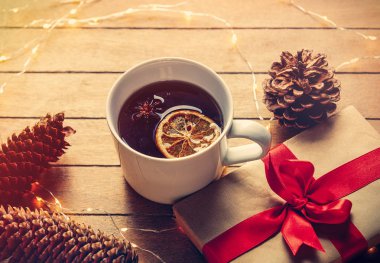 Fincan çay ve çam kozalakları ve peri ışıkları ile Noel kutu hediye ahşap arka plan üzerinde