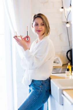 Beyaz beyaz gömlek ve mavi jeans olan kadın makyaj kozmetik bir mutfak.