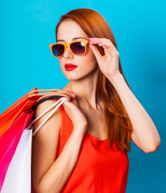 Alışveriş torbaları üzerinde mavi arka plan tutan tarzı Kızıl saçlı kadın.