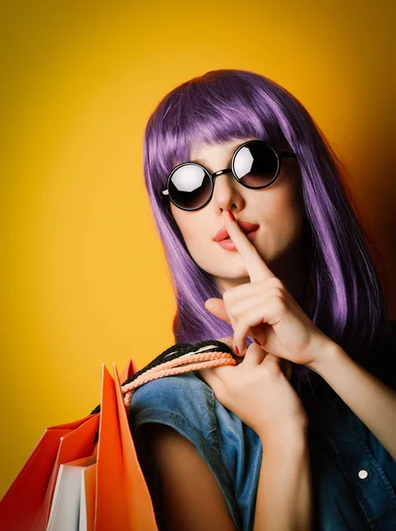 紫の髪とサングラスに黄色の背景に買い物袋を持つ女性 — ストック写真