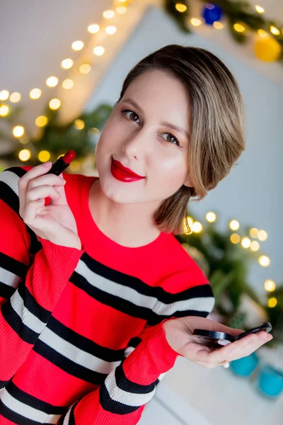 Beautiful woman in red sweater applying lipstick — Stock Photo, Image