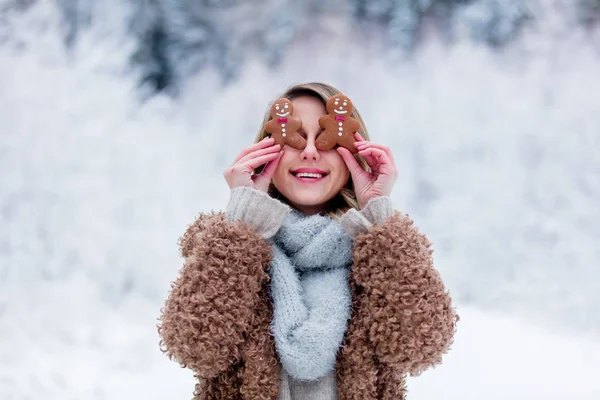 Hermosa chica en abrigo con galleta en un bosque de nieve —  Fotos de Stock