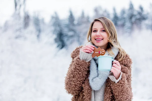Chica con abrigo con taza de bebida caliente y galletas en un bosque de nieve —  Fotos de Stock