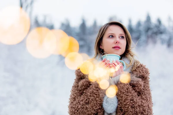 Flicka i rock med kopp varm dryck i en snöskog — Stockfoto