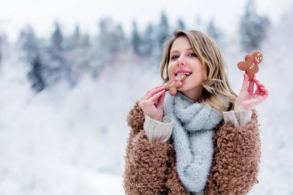 Beautiful girl in coat with cookie in a snow forest — Stock Photo, Image