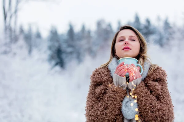 Flicka i rock med kopp varm dryck i en snöskog — Stockfoto