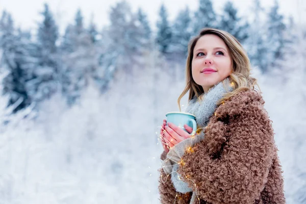 Dziewczyna w płaszczu z filiżanką napoju w lesie śnieżnym — Zdjęcie stockowe