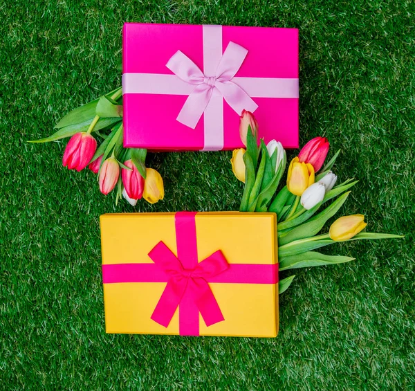 Dárkové krabičky a tulipány na zelené trávě trávníku — Stock fotografie
