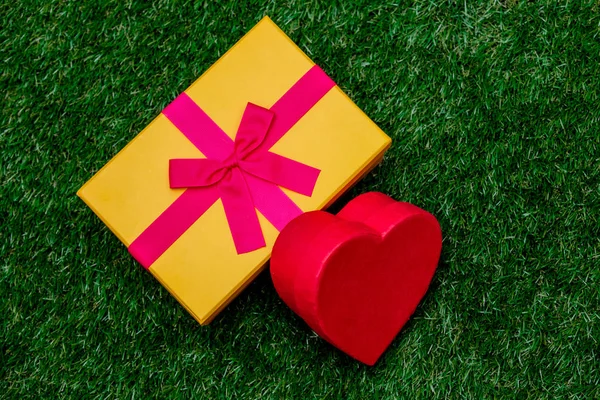 Geschenkbox mit rosa Schleife und Herzform auf grünem Rasen — Stockfoto