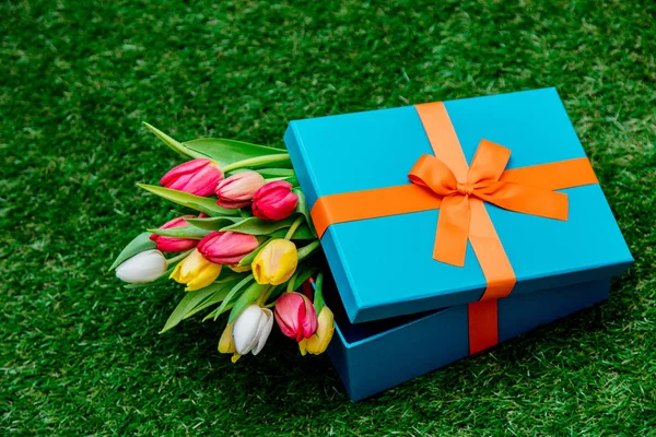 Caja de regalo azul y tulipanes en césped de hierba verde —  Fotos de Stock