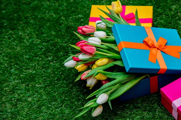 Dárkové krabičky a tulipány na zelené trávě trávníku — Stock fotografie