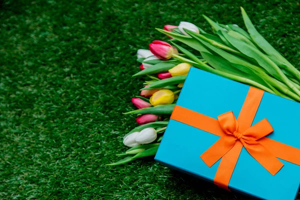 Modrá Dárková krabice a tulipány na zelené trávě trávníku — Stock fotografie